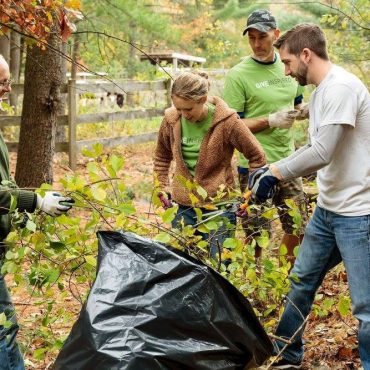a group of people in the woods removing branches and vines and putting them into a black trash bag