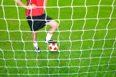 Soccer player with ball standing at goal net
