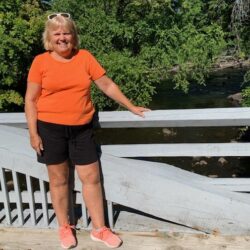 Kathy Hirbour staff member by bridge overlooking river with trees