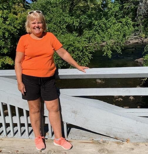 Kathy Hirbour staff member by bridge overlooking river with trees