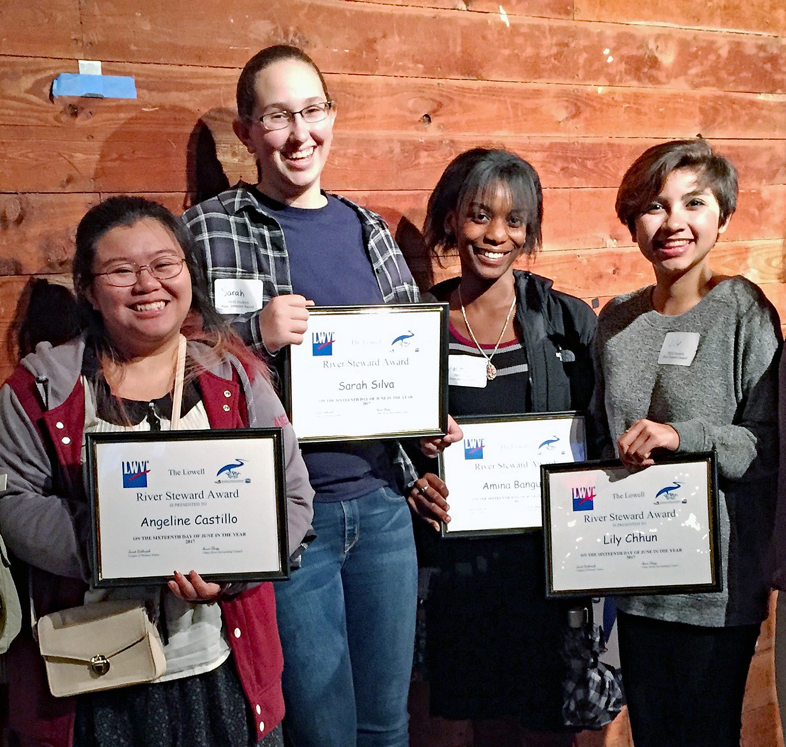 5 high school students hold up "River Steward Awards", smiling by a wooden plank wall