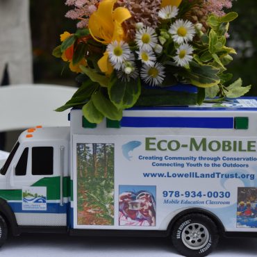 small model ambulance with "Eco Mobile, photos of youth and rafting" table decoration. Flowers on top of truck