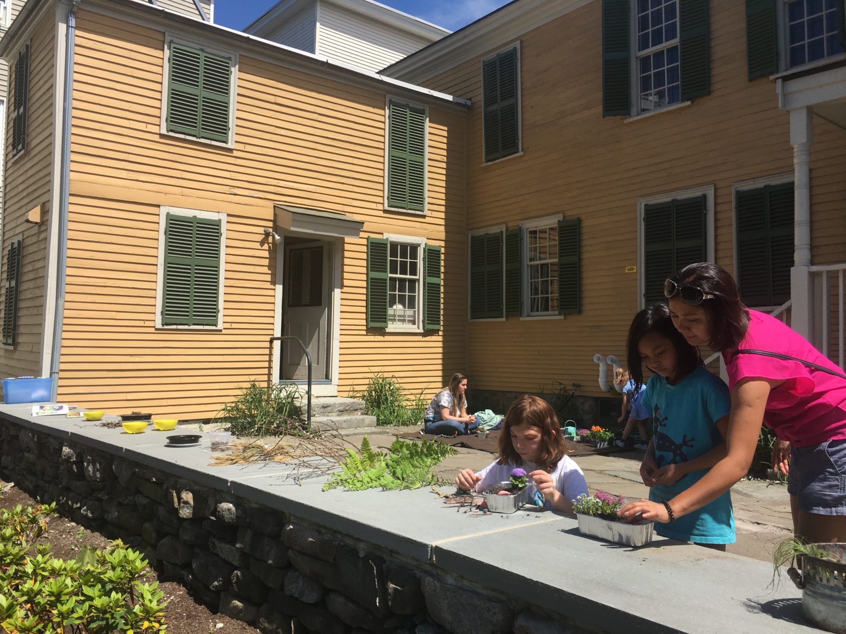 families use leaves, flowers and natural items to make fairy gardens on the patio behind the spalding house, mustard yellow house with dark green shutters