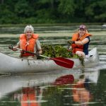 two people in a metal canoe with a full canoe of water chesnut, smiling and rowing on water