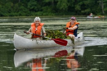 two people in a metal canoe with a full canoe of water chesnut, smiling and rowing on water