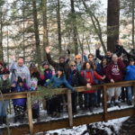 Group of people of all ages posing on a bridge in winter, smiling arms in the air