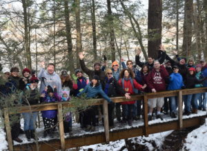 Group of people of all ages posing on a bridge in winter, smiling arms in the air