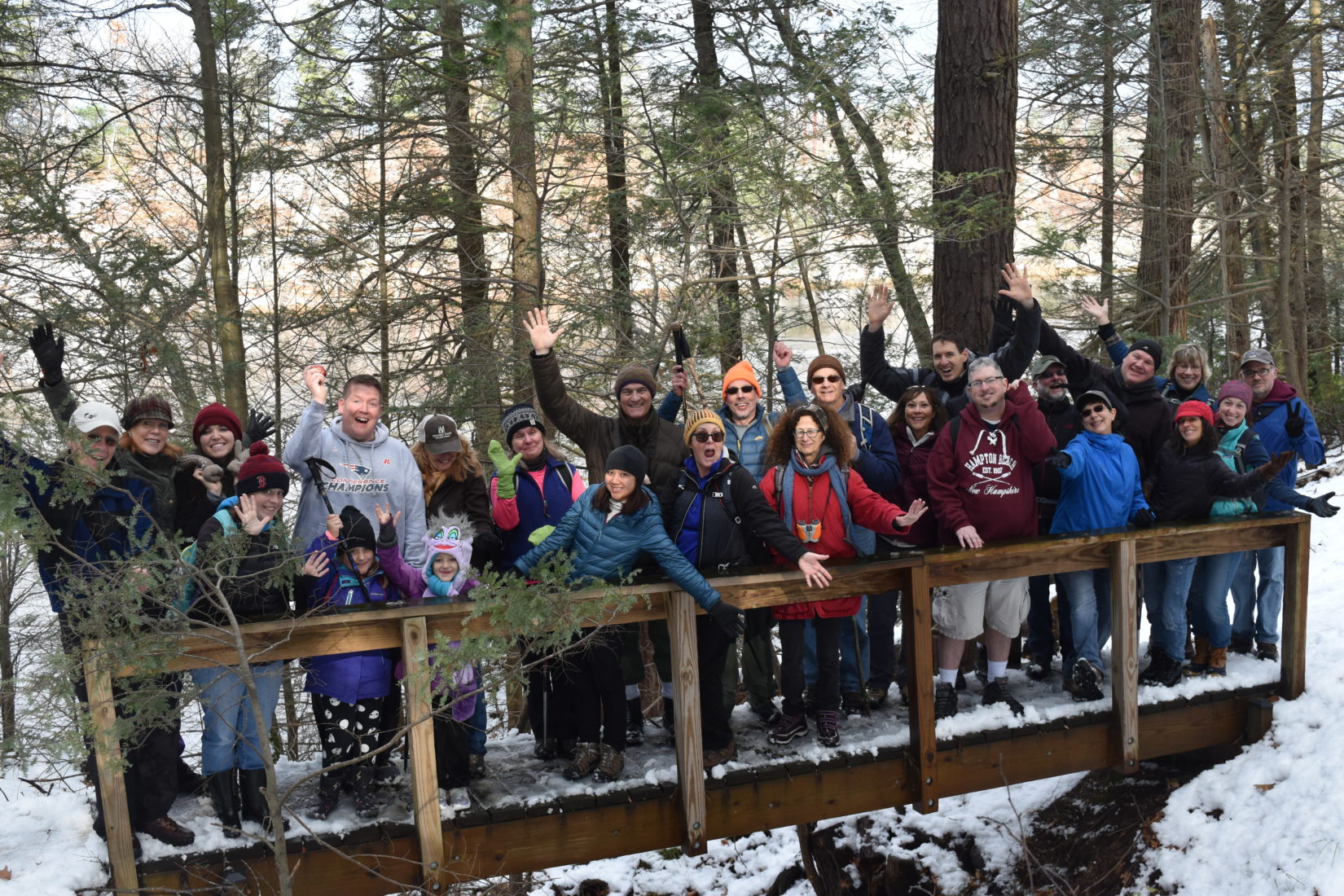 Group of people of all ages posing on a bridge in winter, smiling arms in the air