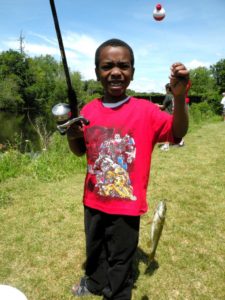 young boy holds up a fishing pole and caught fish by the river