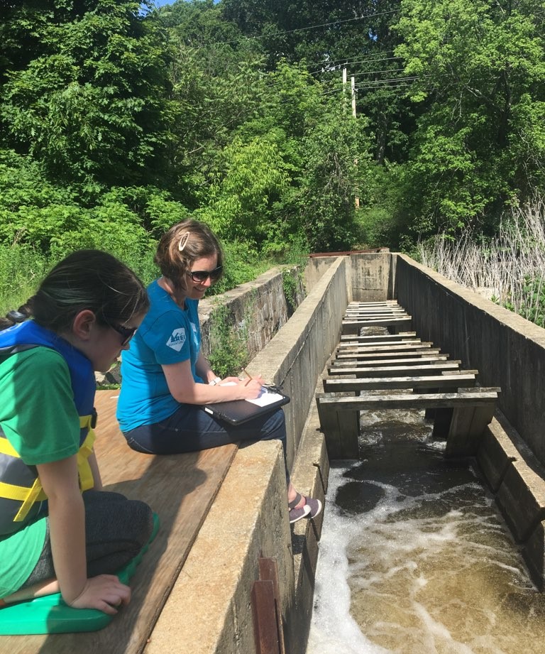 A woman and her daughter sit at the edge of a fish ladder in summer