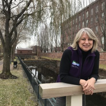 Sheila Kirschbaum LP&CT president smiling by a Lowell canal and willow tree