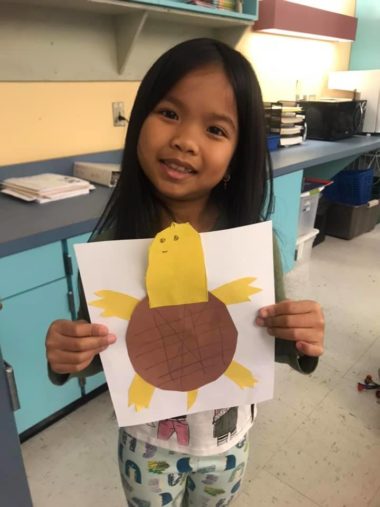 a young girl smiles and holds up a turtle made out of construction picture