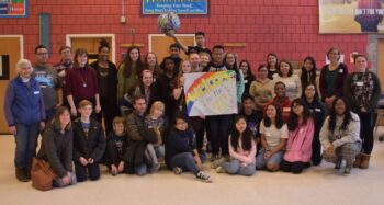 large group of teens and adult mentors pose for a photo, a student holds up a globe, another holds a sign "Welcome to the 2019 EYC"