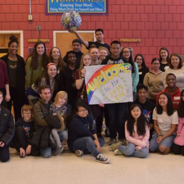 large group of teens and adult mentors pose for a photo, a student holds up a globe, another holds a sign "Welcome to the 2019 EYC"