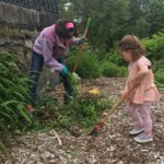 mother and young girl rake mulch and pull weeds